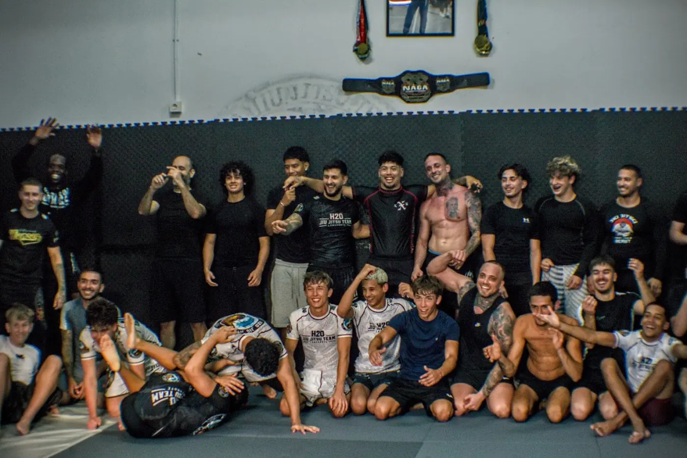 Foto de grupo del equipo H2O celebrando al final de un entrenamiento, bajo un cinturón de campeonato NAGA.